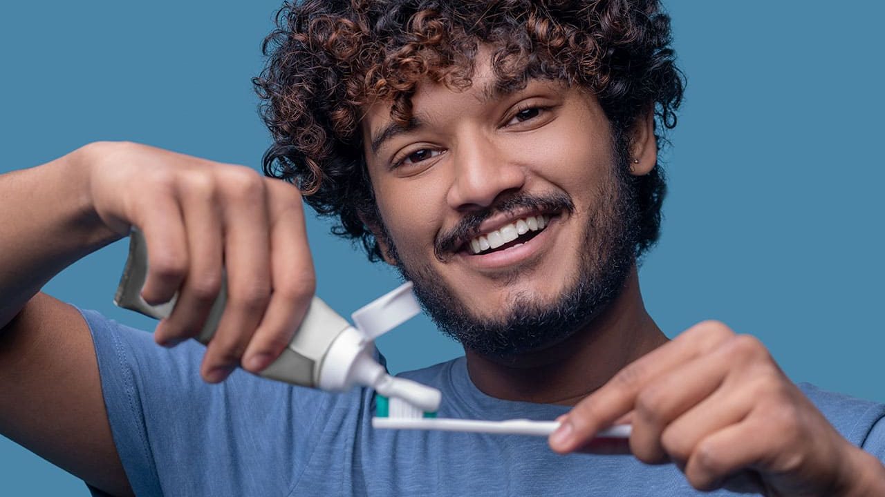 pessoa sorrindo e mostrando uma escova de dentes com creme dental